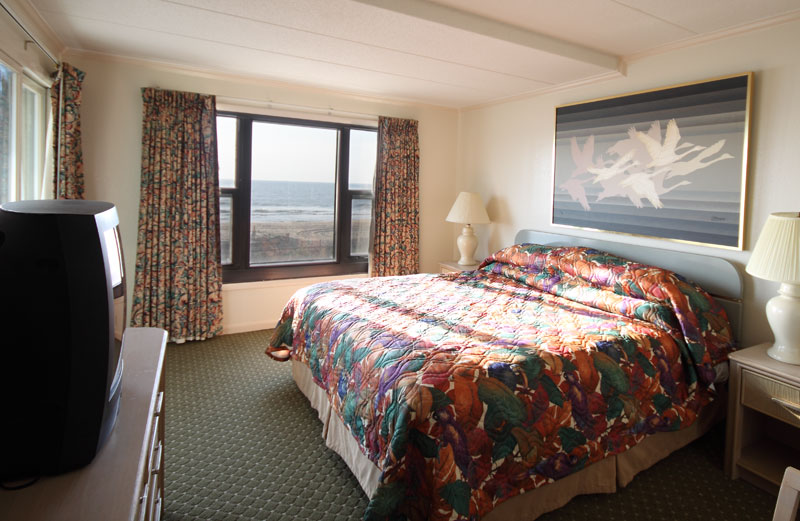 A master bedroom with a king bed, tv and ocean view.